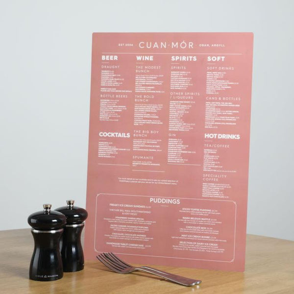 A portrait image of a pink and white long lasting SuperTuffMenu beside the menu sits some cutlery and salt and peppers grinder to give the size context