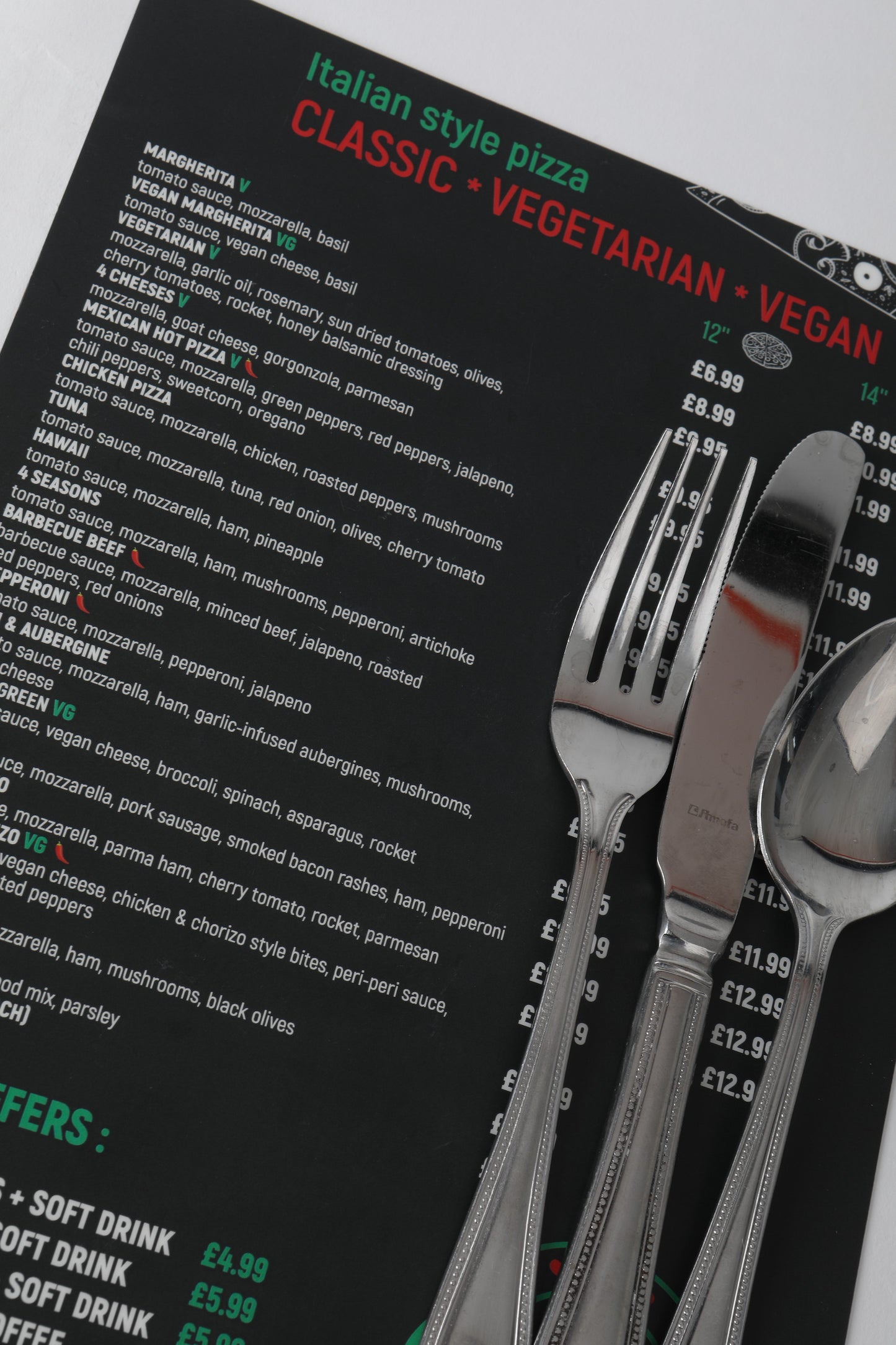 Section of menu black background with white green and red text with cutlery for scale